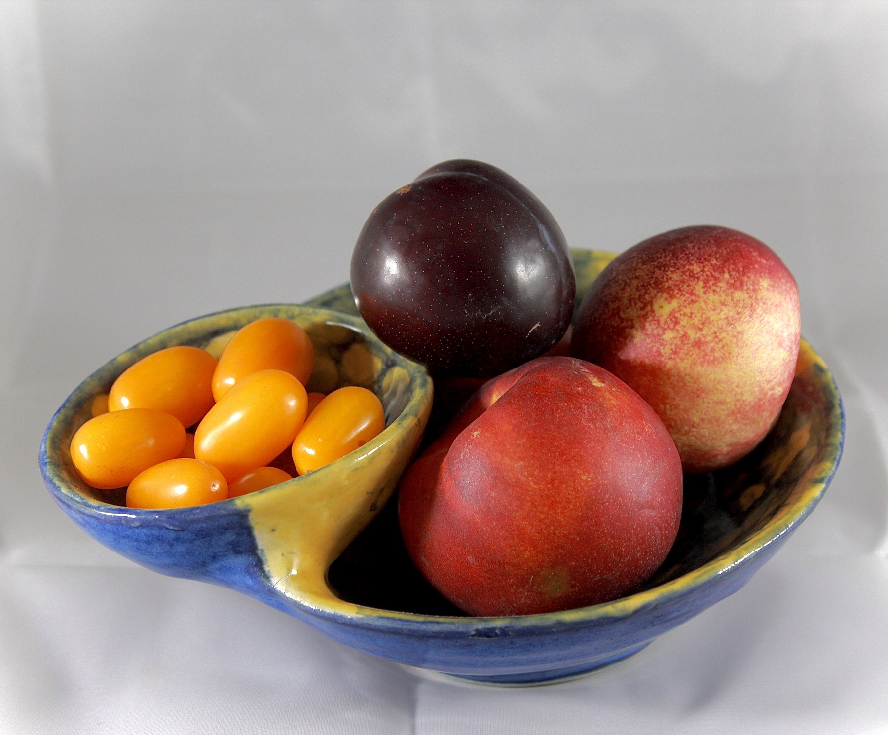 Blue and yellow ceramic chip-and-dip bowl displayed with fruit and small tomatoes