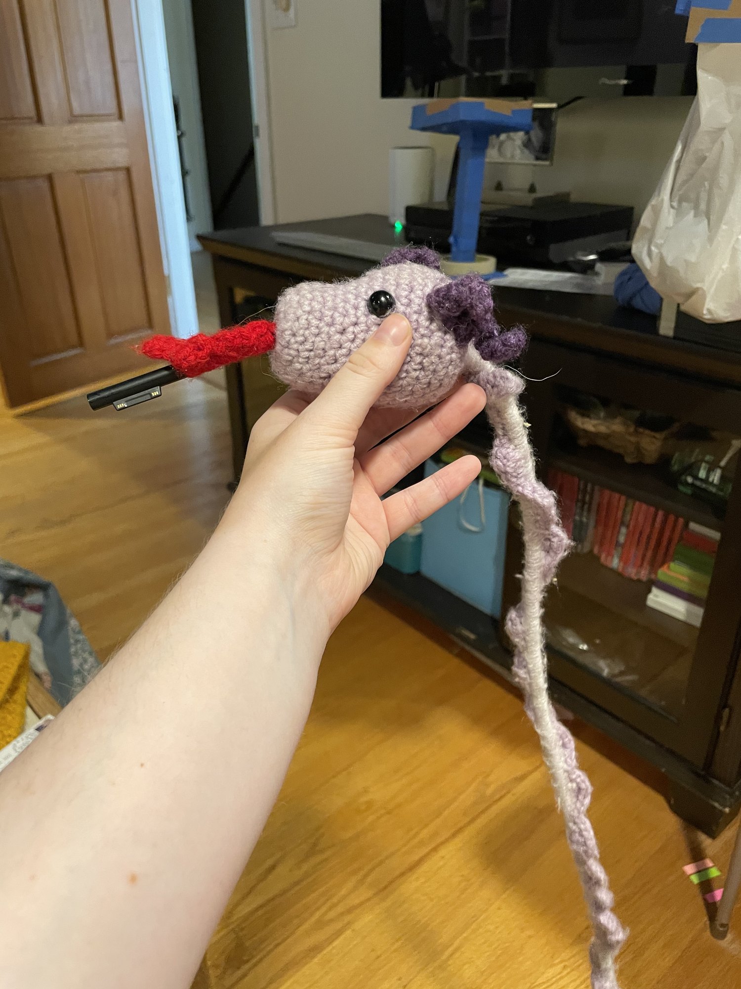 Small crocheted creature with a long tail, held in one hand