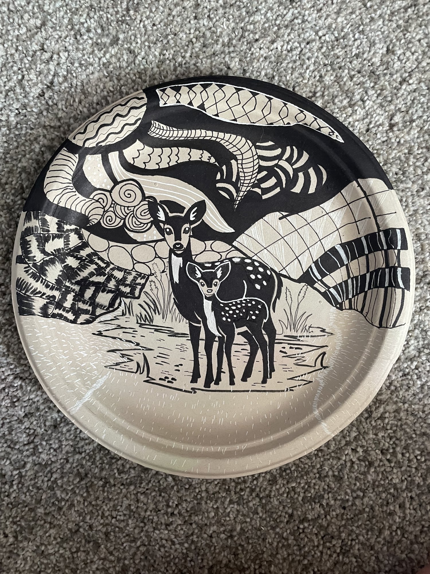 Black and white zentangle-style ink drawing of two deer in a patterned landscape, on a round plate