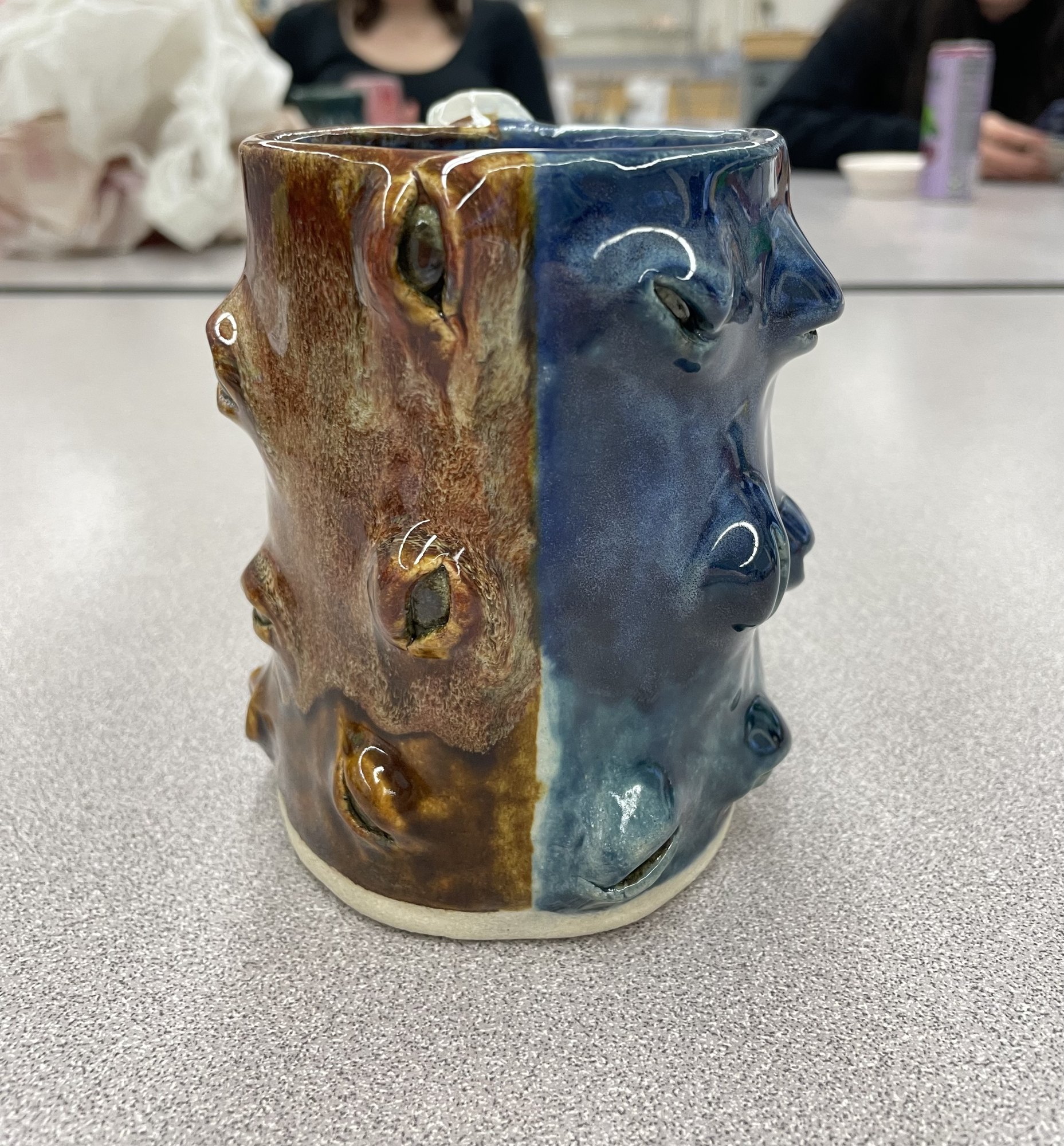 Ceramic vessel with faces pressed into the surface, glazed brown on one half and blue on the other